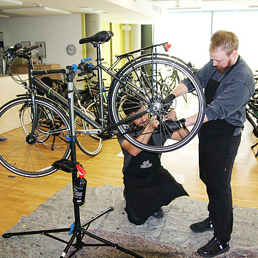 Fahrradcheck bei Projektron: Wartung durch das Zweirad-Team Zweiradprofis führen einen Fahrradcheck durch und warten ein Fahrrad, indem sie Bremsen und Kette überprüfen.